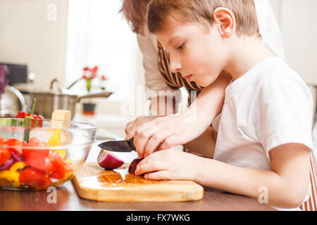 Petit garçon en tranches de coupe légumes pour salade avec sa mère dans la cuisine cuisine familiale contexte Banque D'Images