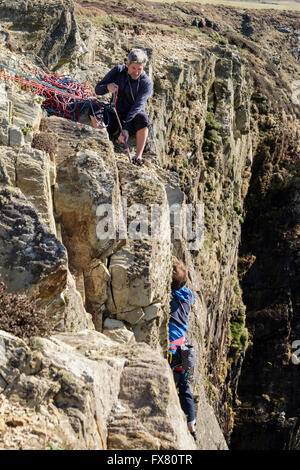 Rock climber belayed plomb en haut de falaises côtières Gogarth l'assurage second grimpeur ci-dessous. L'Île Sainte de South Stack Anglesey Pays de Galles Banque D'Images