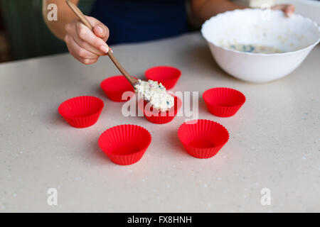 Jeune femme met la pâte dans des formes de muffins dans la cuisine Banque D'Images