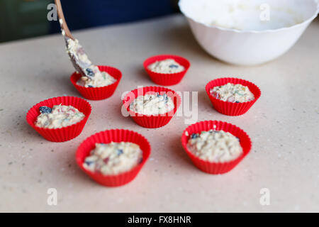 Jeune femme met la pâte dans des formes de muffins dans la cuisine Banque D'Images