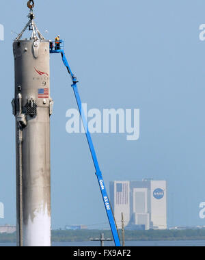 Port Canaveral, Floride, USA. 12 avril, 2016. Travailleurs d'un ascenseur, d'examiner la première étape d'une fusée SpaceX Falcon 9 à Port Canaveral, Floride après que le Rocket a été retourné au port pendant la nuit sur un drone barge. La fusée a atterri avec succès sur la barge pour la première fois le 8 avril 2016 après avoir été lancée de Cap Canaveral avec un dragon spacecraft sur une mission de ravitaillement pour la Station spatiale internationale. SpaceX espère pouvoir réutiliser la fusée dans les mois à venir. Véhicule de la NASA d'assemblage est vu dans la distance. Crédit : Paul Hennessy/Alamy Live News Banque D'Images