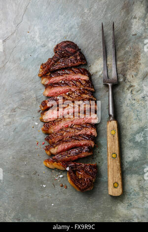 Tranches de boeuf grillé bifteck de contre-filet barbecue Fourchette à viande et sur fond ardoise gris Banque D'Images