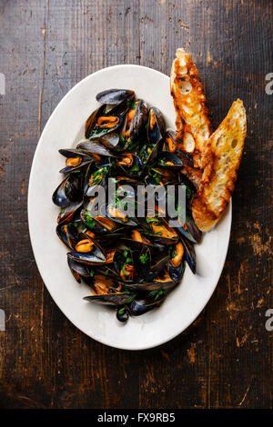 Moules au persil et toasts de pain sur la plaque sur fond de bois foncé Banque D'Images