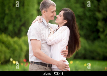 Couple d'amoureux sur une date dans le parc, debout face à face, jeune homme embrassant tendrement son happy smiling girlfriend Banque D'Images