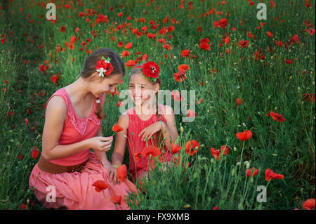 Deux jeunes filles en robe rouge marche sur champ de coquelicots Banque D'Images