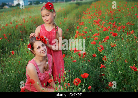 Deux jeunes filles en robe rouge marche sur champ de coquelicots Banque D'Images