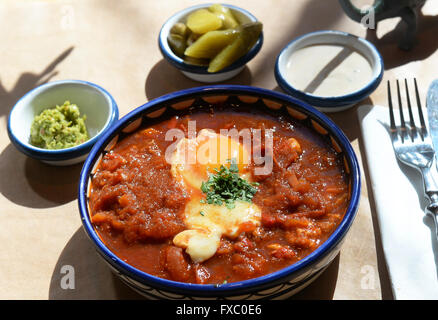 Shakshuka, un plat d'œufs traditionnel israélien, est assis sur une table avec des côtés au Café Gordon dans le quartier de Neukölln à Berlin, Allemagne, 01 avril 2016. Le plat est fait avec les oeufs pochés dans une sauce à base de tomates, poivrons, piments, et les oignons. En plus des plats israéliens, les propriétaires du café, originaire de Tel Aviv, vendent aussi leur Legothek records off label. Photo : Jens Kalaene/dpa Banque D'Images