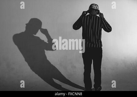 Un homme portant un chapeau, debout avec son dos à la caméra avec son ombre sur le mur. Banque D'Images