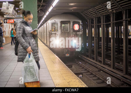 Une femme préoccupée par son smartphone en tant que plate-forme du métro comme un train arrive à New York le lundi 11 avril, 2016. (© Richard B. Levine) Banque D'Images