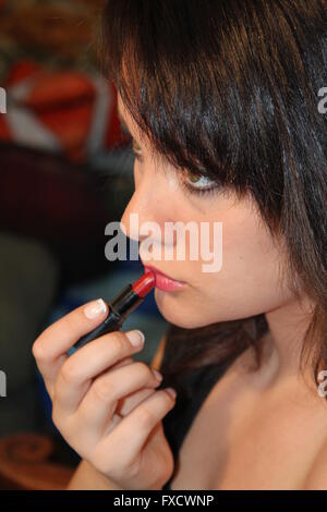 Belle jeune brunette applying lipstick, contre une pièce. Banque D'Images