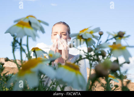 Jeune femme éternuements dans une prairie de fleurs Daisy. Elle est allergique aux fleurs Banque D'Images