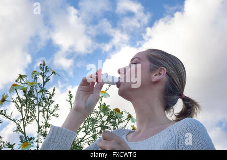 Jeune femme à l'aide d'inhalateur pour le traitement de l'asthme allergique au pré des fleurs Banque D'Images