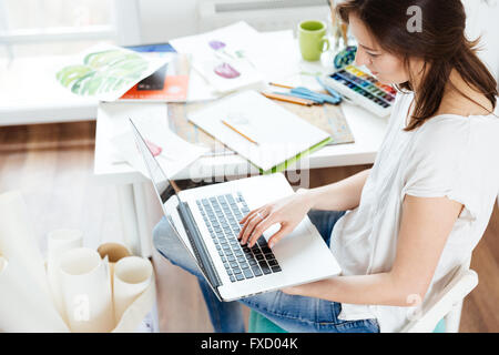 Belle femme artiste sitting and using laptop in workshop Banque D'Images