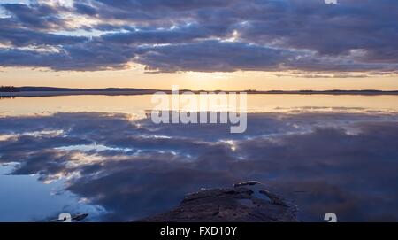 Nuages spectaculaires et des couleurs éclatantes de coucher du soleil à un lac en Finlande une calme soirée de printemps. Le soleil est juste derrière les nuages rea Banque D'Images