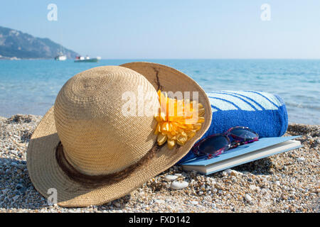 Lunettes de soleil chapeau de paille, serviette et livre sur une plage Banque D'Images