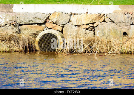 Déduits d'eaux pluviales en sortie d'une rivière avec des blocs de pierre et d'une partie d'une pelouse au-dessus. Banque D'Images