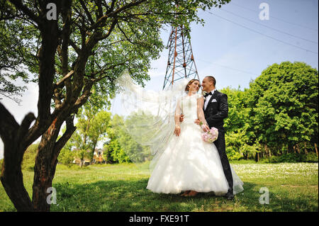 Happy wedding couple à la mode tour électrique de fond à l'autre, le vent jouer avec voile de mariée Banque D'Images