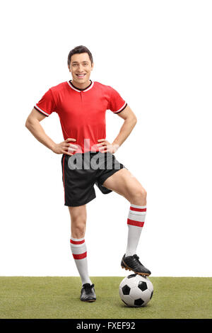 D'un coup vertical joueur de football en un maillot rouge enjambant une boule sur une surface d'herbe isolé sur fond blanc Banque D'Images