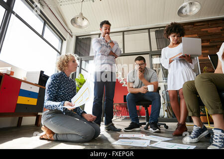 Équipe de créatifs ayant une réunion avec woman holding documents. Groupe de jeunes créateurs siégeant ensemble travailler sur de nouveaux Banque D'Images