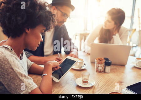 Close up portrait of young woman using digital tablet avec ses amis assis à une table de café. Groupe de jeunes Banque D'Images