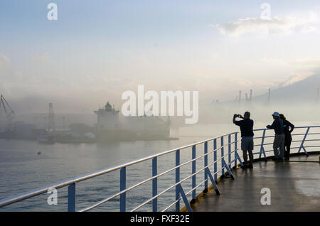 Les touristes debout sur le pont des navires de croisière dans le port de Naples en Italie sur un matin brumeux. Banque D'Images