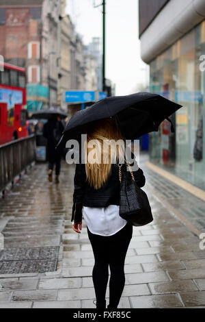 Femme avec de longs cheveux blonds holding umbrella sous la pluie à Londres Banque D'Images