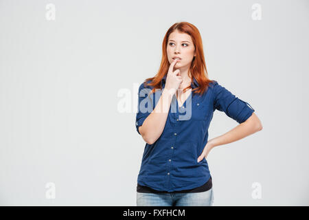 Thoughtful redhead jolie jeune femme debout et de penser sur fond blanc Banque D'Images