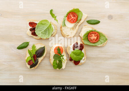 Des sandwichs ouverts de ciabatta, tomates séchées au soleil, fromage crémeux, roquette et basilic feuille de laitue. Antipasti Banque D'Images