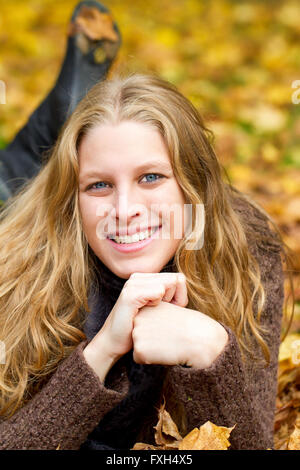 Young woman lying on prairie avec les feuilles d'automne Banque D'Images