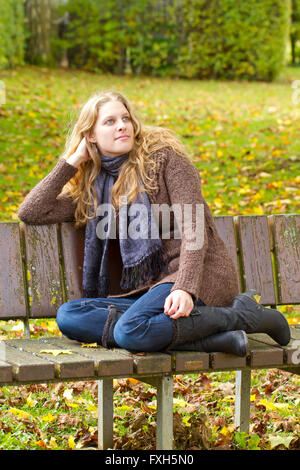 Jeune femme assise sur le banc de parc en automne Banque D'Images