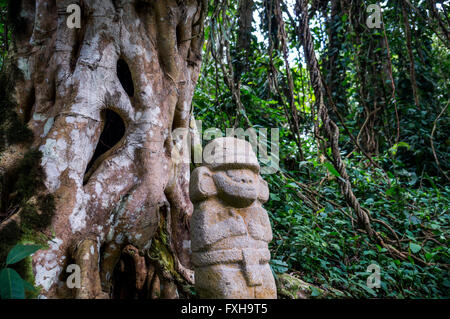 Une mystérieuse statue d'un homme qui se trouve dans la forêt à côté d'un vieil arbre avec de grandes racines. L Banque D'Images