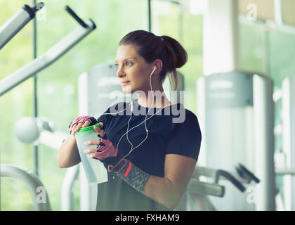 Femme avec un casque et de l'eau potable au repos at gym Banque D'Images