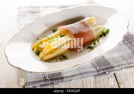 L'asperge blanche fraîchement cuit avec du beurre fondu, jambon séché à l'air et le persil haché sur une plaque Banque D'Images