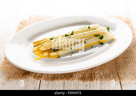 L'asperge blanche fraîchement cuit avec du beurre fondu et le persil haché sur une plaque Banque D'Images