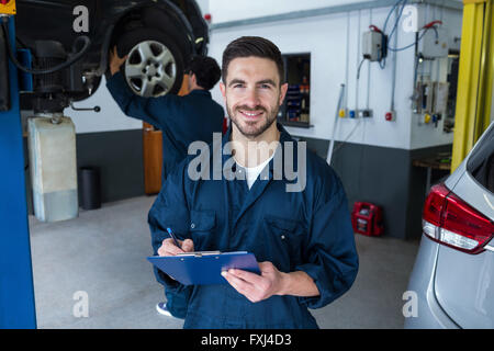 La préparation d'un mécanicien de vérifier liste alors qu'une collègue de réparer des véhicules Banque D'Images