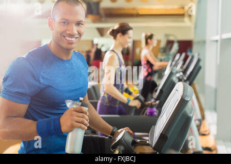 Portrait of smiling man avec de l'eau bouteille sur tapis roulant à la salle de sport Banque D'Images
