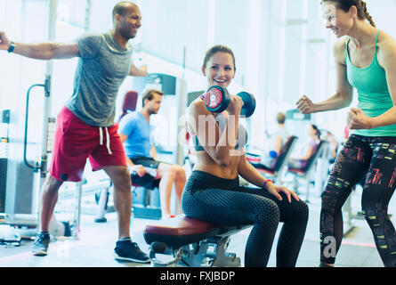 Woman cheering sur ami faisant haltère biceps at gym Banque D'Images