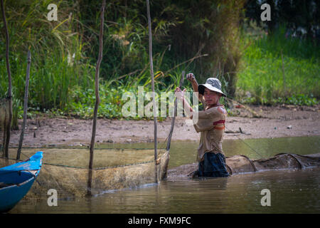 Vietnamese homme debout dans l'eau statique fixation des filets de pêche utilisés pour la reproduction des poissons, Chau Doc, Vietnam Banque D'Images