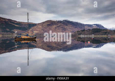Un vieux bateau à voile parfaitement reflétée dans les eaux calmes du Loch Leven. Banque D'Images