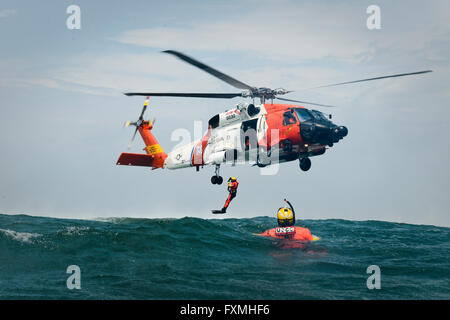 Un garde-côte des nageurs sont déployées à partir d'un hélicoptère Jayhawk MH-60 au cours de la formation en sauvetage dans l'Océan Atlantique le 23 juin 2015 près de Cape Cod, au Massachusetts. Banque D'Images