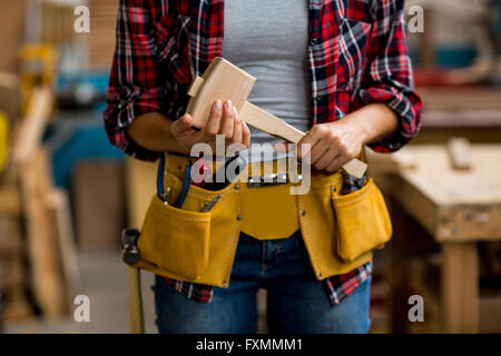 Mid section of woman holding mallet avec ceinture d'outils autour de sa taille Banque D'Images