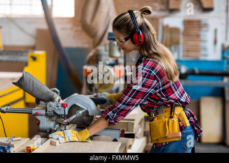 Female carpenter avec planche en bois de coupe scie électrique Banque D'Images