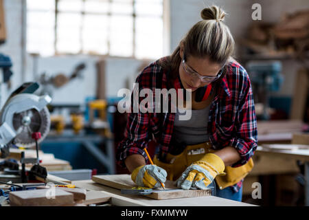 Female carpenter marquage sur planche en bois avec un crayon Banque D'Images