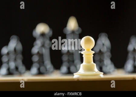 Le pion blanc debout devant l'équipe d'échecs noir Banque D'Images