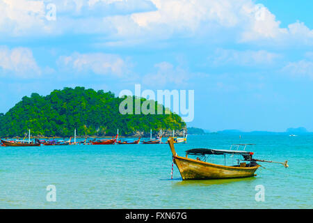 Bateau à longue queue thaïlandais ancrée dans l'eau bleu ciel avec le plus de bateaux à longue queue et une falaises couverts vert dans l'arrière-plan. Banque D'Images