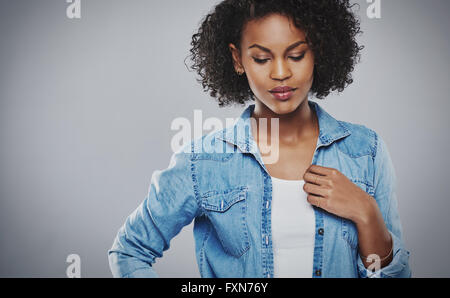 Jolie pensive African American Woman avec une coiffure afro curly debout avec sa main à sa poitrine en regardant le sol Banque D'Images