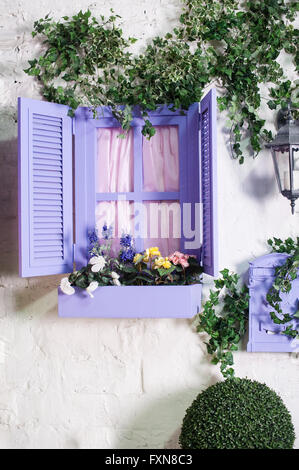 Jolie petite fenêtre mauve et fort avec des fleurs dans une maison ancienne Banque D'Images