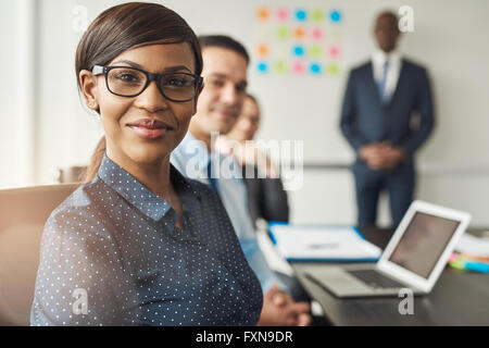 Belle femme professionnelle joyeuse portant des lunettes assis avec leurs collègues masculins et de chef d'équipe dans la salle de conférence au travail Banque D'Images