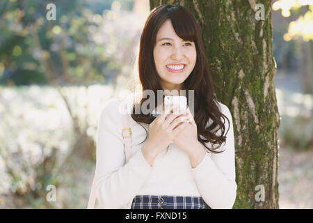 Jeune japonaise avec le smartphone dans un parc de la ville Banque D'Images