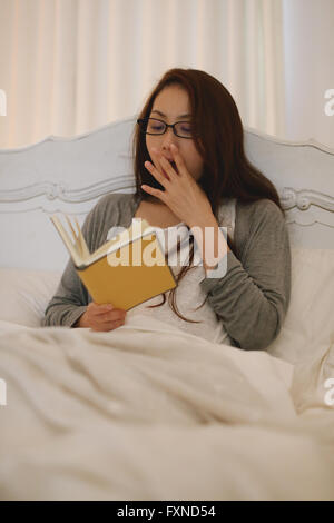 Jeune femme japonaise attrayant lire au lit Banque D'Images